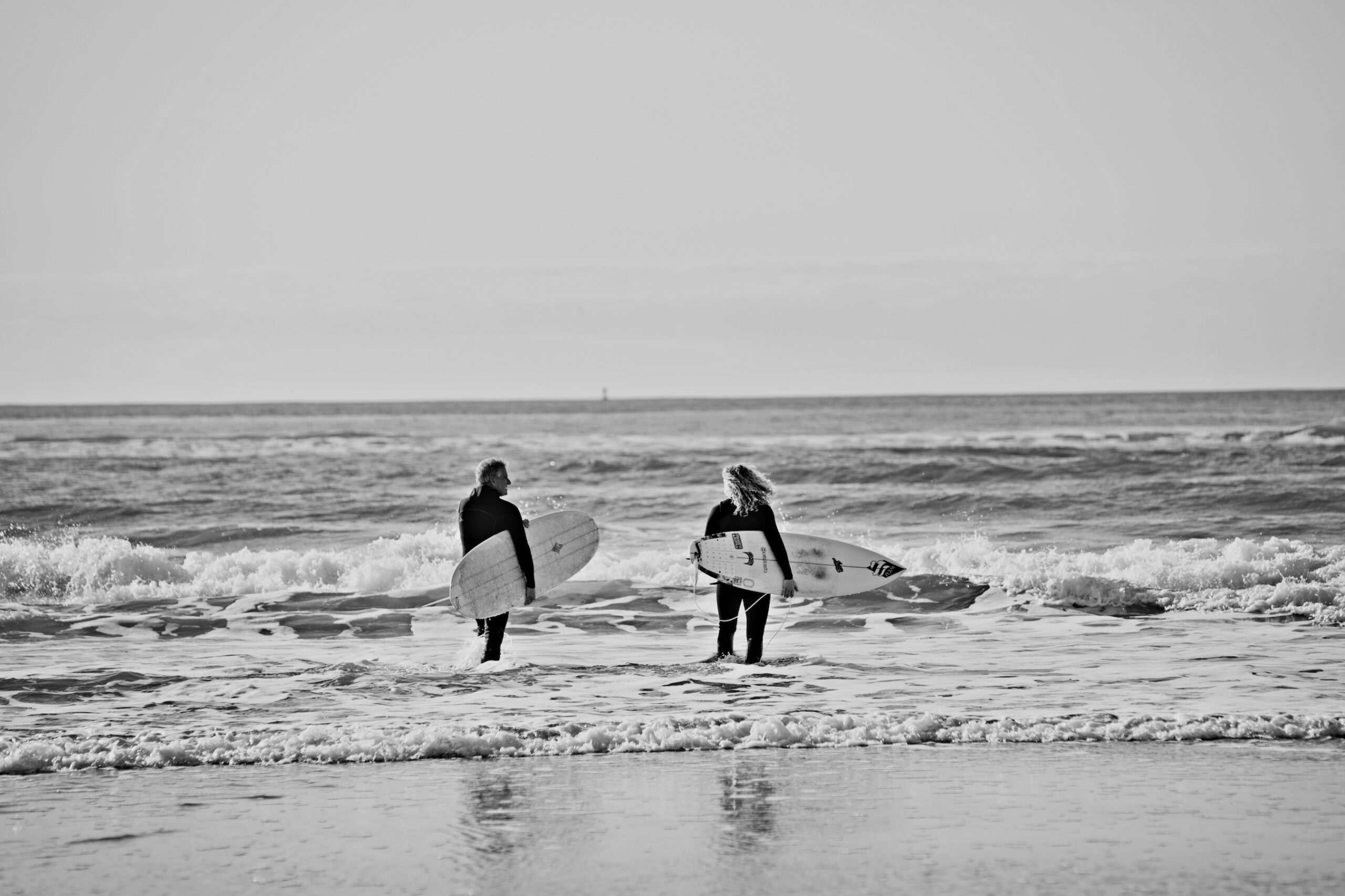 two surfers walking through waves with boards under arms