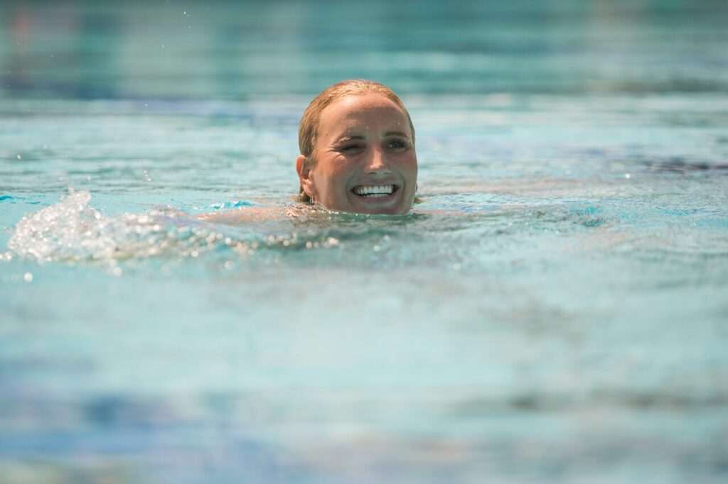 A person is smiling while swimming in a clear, blue body of water, enjoying the great outdoors reminiscent of a refreshing day in Sonoma.