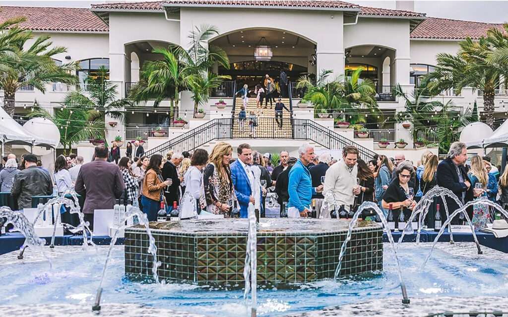 People mingling and drinking wine at a hotel by the fancy water fountain in the courtyard