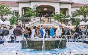 People mingling and drinking wine at a hotel by the fancy water fountain in the courtyard