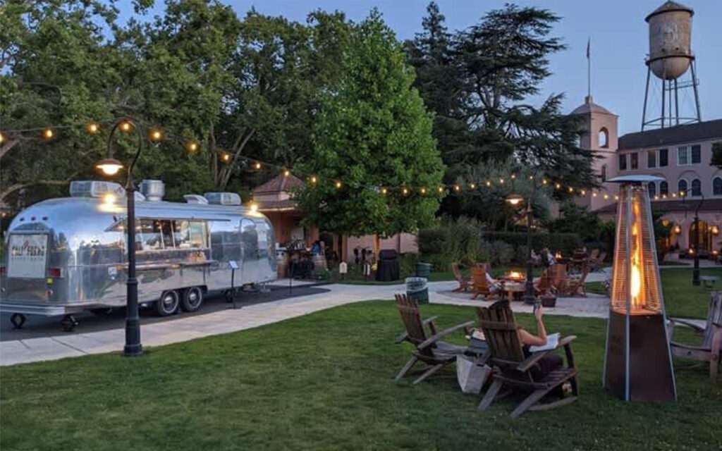 Airstream food truck and people enjoying themselves around fire pits outside of a hotel on the front lawn.