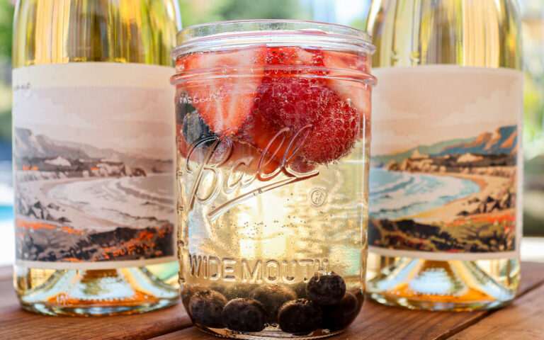 up close image of two wine bottles and a bubbly mocktail with fresh fruit